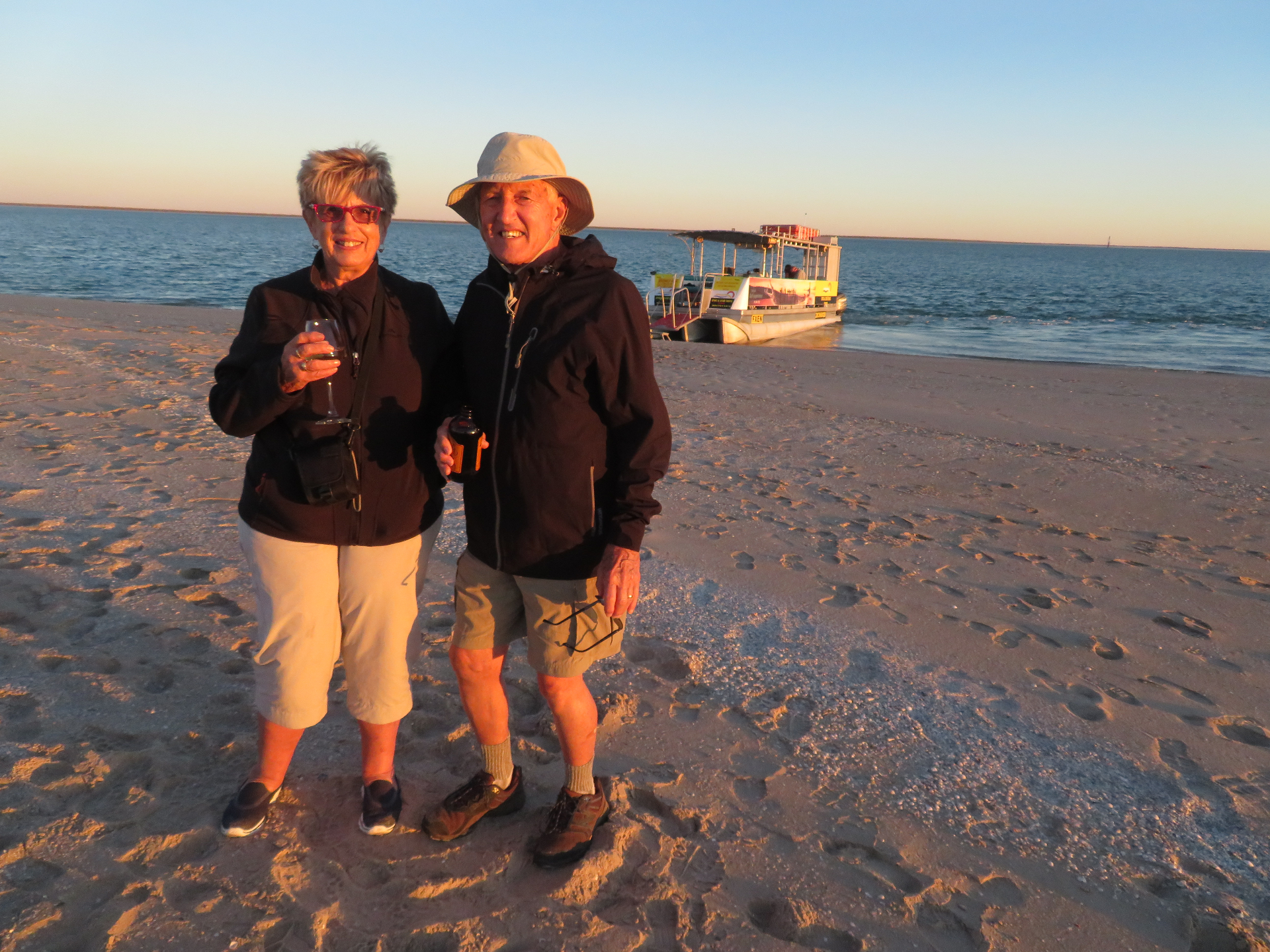 Ron and Kay Pitcher on a beach at sunset with a boat in the background