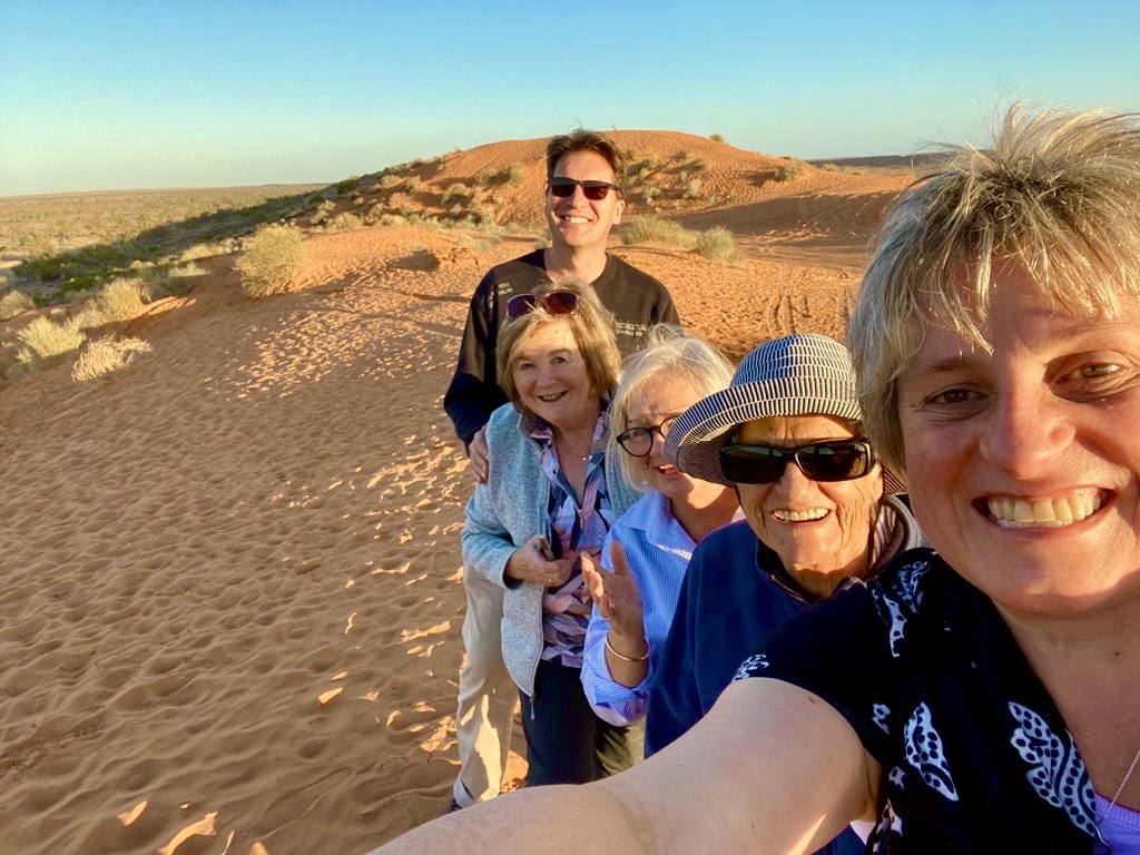 Group of Air Adventure guests smiling on a red sand dune at sunset